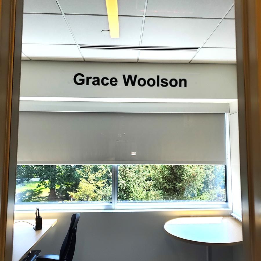View of Grace’s office with her nametag, desk and chair, guest table, and window to the outside.