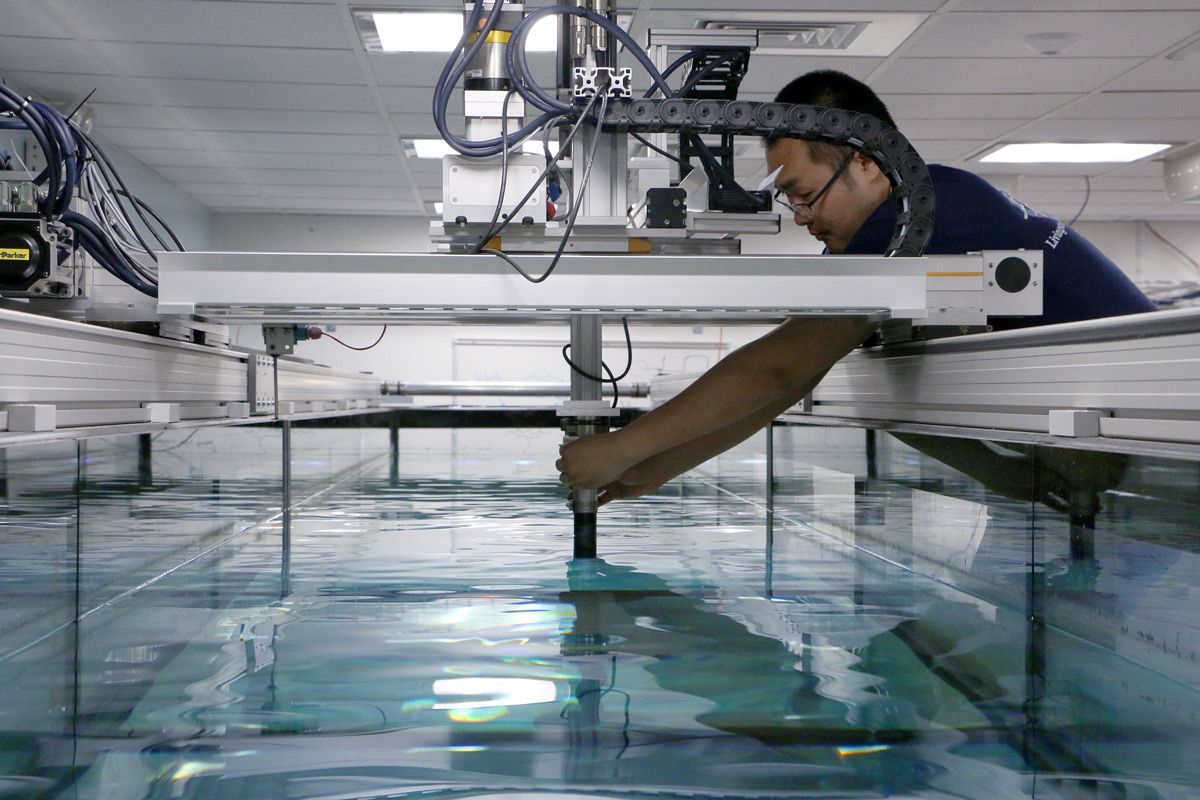 Dr. Fan leans over the edge of the tank to adjust the robot.